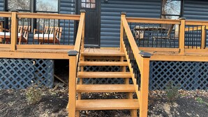 Eine Holzterrasse mit einer Treppe zu einer Hütte mit großen Fenstern und einer Tür.