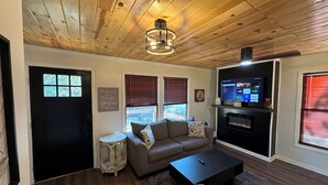 Ein Wohnzimmer mit Holzboden, einer schwarzen Tür, einem grauen Sofa, einem schwarzen Couchtisch und einem Fernseher auf einem schwarzen Lowboard.