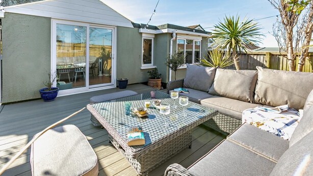 Een overdekt terras met een rieten tafel, een bank en een eethoek.