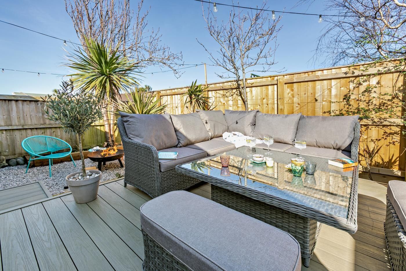 An outdoor patio with a wicker sofa, a glass-top coffee table, and a teal chair.
