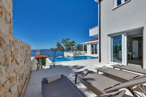 Un edificio moderno con piscina, mobiliario exterior y vista al mar.