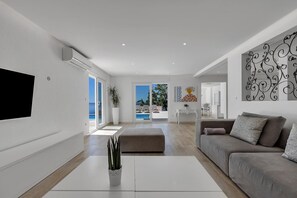 A modern living room with a flat-screen TV, a sofa, a coffee table, and a view of the outdoors.