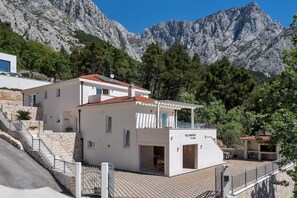 A modern villa with a stone staircase, a balcony, and a mountain backdrop.