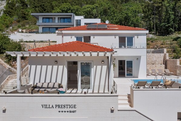 Una villa moderna con piscina, zona de estar exterior cubierta y vistas del paisaje circundante.