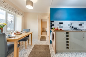 Eine moderne Küche mit blauer Akzentwand, einem Essbereich mit Holztisch und -stühlen sowie Blick auf die Straße.
