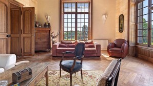 Een kamer met houten vloeren, een piano, een bank, een stoel en een groot raam.