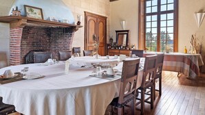 A dining area with a brick fireplace, wooden ceiling, and large windows. - Château du Perray – Princess Room with Park View and Shared Pool (Saint-Mars-du-Désert)