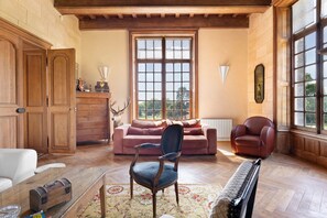 Une pièce avec un plancher en bois, une grande fenêtre, un canapé, un fauteuil, un piano et un meuble.