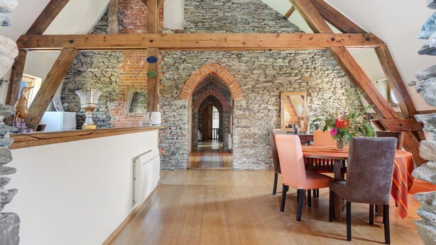A rustic dining area with a stone wall, wooden beams, and a view into a hallway.