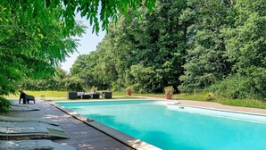 A swimming pool with lounge chairs and a small table, surrounded by dense greenery.