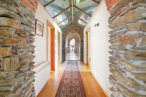 Un couloir aux murs de pierre, doté d’un plancher en bois et d’un tapis à motifs, qui mène à une pièce éclairée par une lucarne.