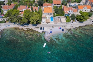 Luftaufnahme einer Küstenlandschaft mit Häusern, einem Strand und klarem Wasser.