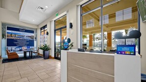 Un área de recepción de diseño moderno, con mostrador de recepción, una zona de estar con sofá y sillones, y un cartel grande que anuncia servicios de administración de alquileres vacacionales.