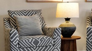 Una silla con estampado en zigzag, una mesita auxiliar redonda de madera y una lámpara con pantalla texturizada.