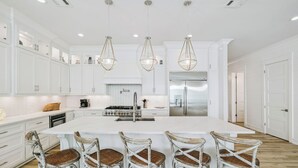 A spacious kitchen with white cabinetry, a large island with bar stools, and pendant lighting. - Ultimate Escape – Spacious Family Home w/ Private Pool & 8 Bikes, 3-Min to Beach (Seagrove Beach)