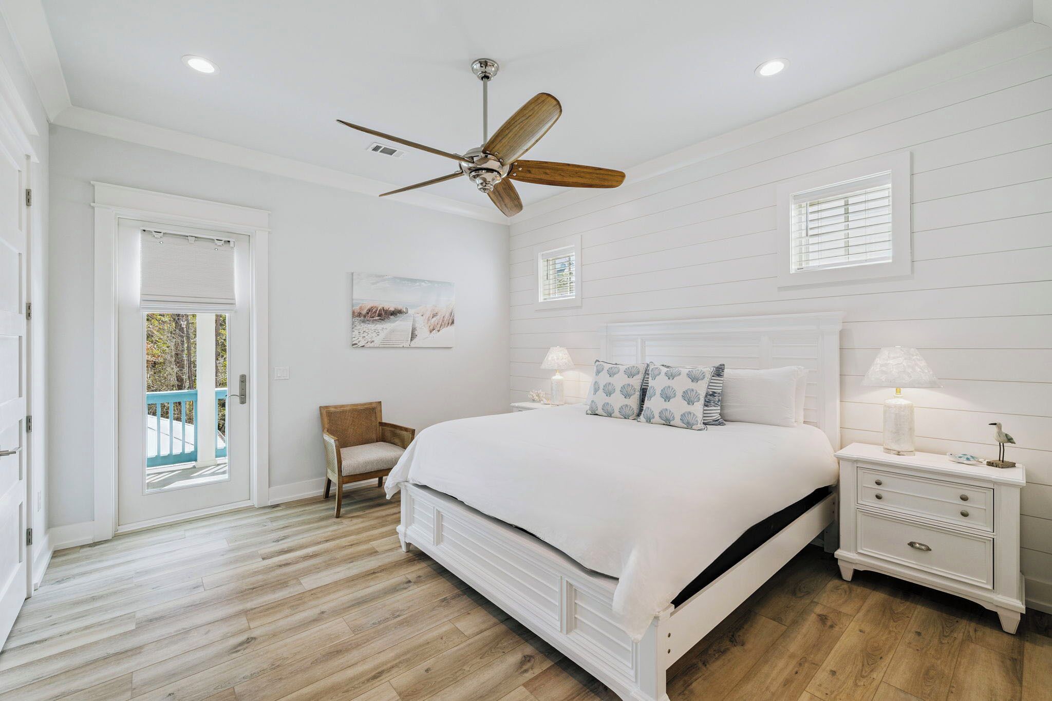 A bedroom with a bed, nightstand, chair, ceiling fan, and a view of the outdoors.