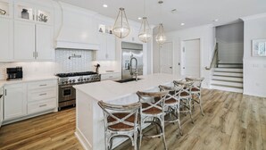 A modern kitchen with white cabinetry, a large island with bar stools, stainless steel appliances, and pendant lighting. - Ultimate Escape – Spacious Family Home w/ Private Pool & 8 Bikes, 3-Min to Beach (Seagrove Beach)
