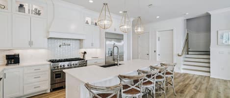 A modern kitchen with white cabinetry, a large island with bar stools, stainless steel appliances, and pendant lighting.