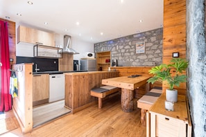 A modern kitchen with wooden cabinetry, a stone accent wall, and a wooden dining table with benches. - Holiday Apartment “Le Télégraphe” with Shared Garden and Wi-Fi (Valloire)