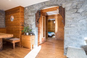 Interior de madera con paredes de piedra, un banco, una mesa y una cama al fondo.