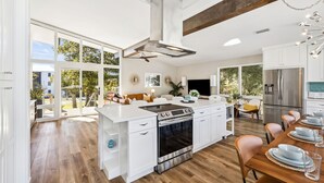 A modern kitchen with white cabinetry, a central island, and a dining area with a wooden table and chairs. - Spacious Family Retreat w/ Pool, LSV, 7 Bikes, & Generous Outdoor Space w/BBQ (Dune Allen)