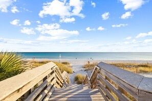 Une promenade en bois menant à une plage, avec un ciel dégagé et une mer calme.