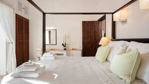 A bedroom with a large bed, a bedside table, a mirror, a wooden wardrobe, and a bathroom visible through an open door. - Spartilas Villas (Corfu)