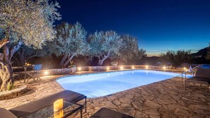A swimming pool with stone flooring, surrounded by olive trees and outdoor seating. - Spartilas Villas (Corfu)