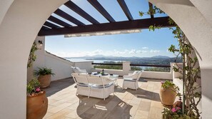 Eine Terrasse mit einer Pergola, Korbmöbeln und Topfpflanzen.