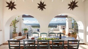 A dining area with a table set for six, surrounded by arches with potted plants, and star-shaped wall decorations. - Spartilas Villas (Corfu)