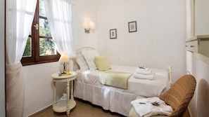 A bedroom with a single bed, a bedside table with a lamp, a chair, and two framed pictures on the wall. - Spartilas Villas (Corfu)