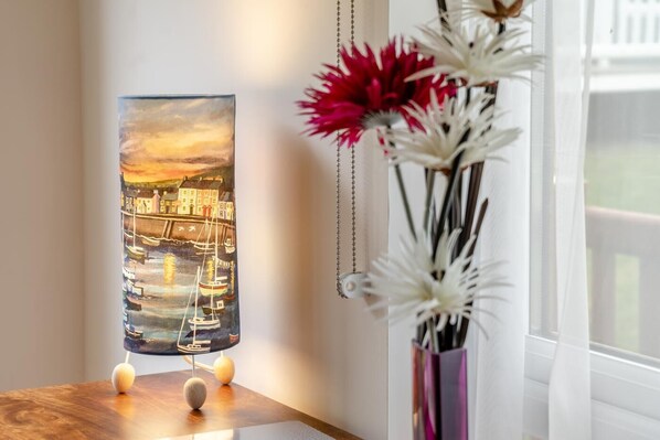 A painting of a harbor scene with boats and buildings, a vase with flowers, and a wooden table.