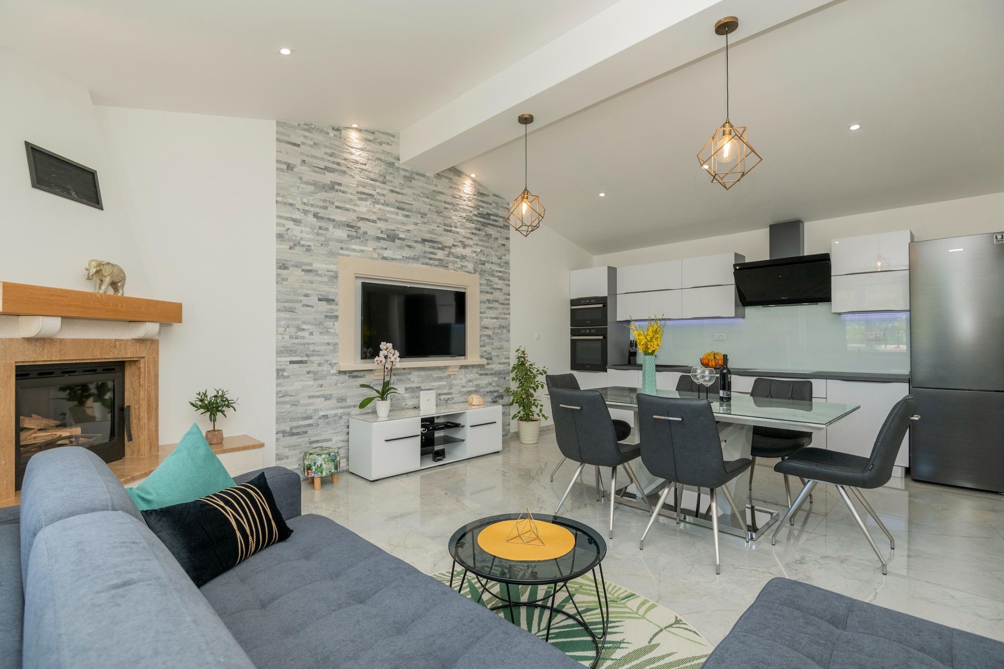 A modern living room with a fireplace, grey sofa, and a dining area with chairs and a table.