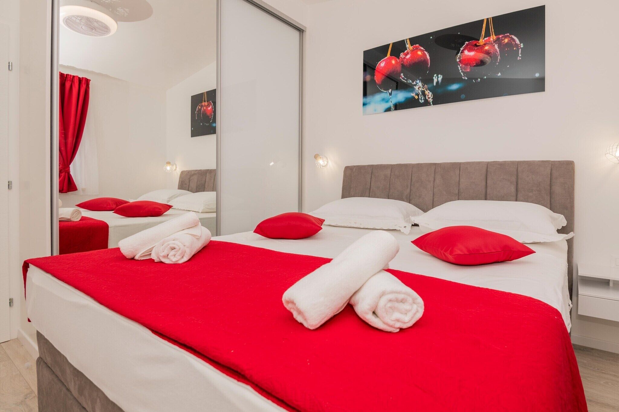 Une chambre d’hôtel avec un lit, une literie rouge et blanche, un grand miroir et une œuvre d’art accrochée au mur.