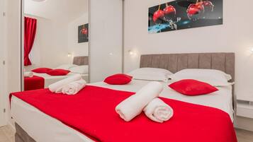 Une chambre d’hôtel avec un lit, une literie rouge et blanche, un grand miroir et une œuvre d’art accrochée au mur.