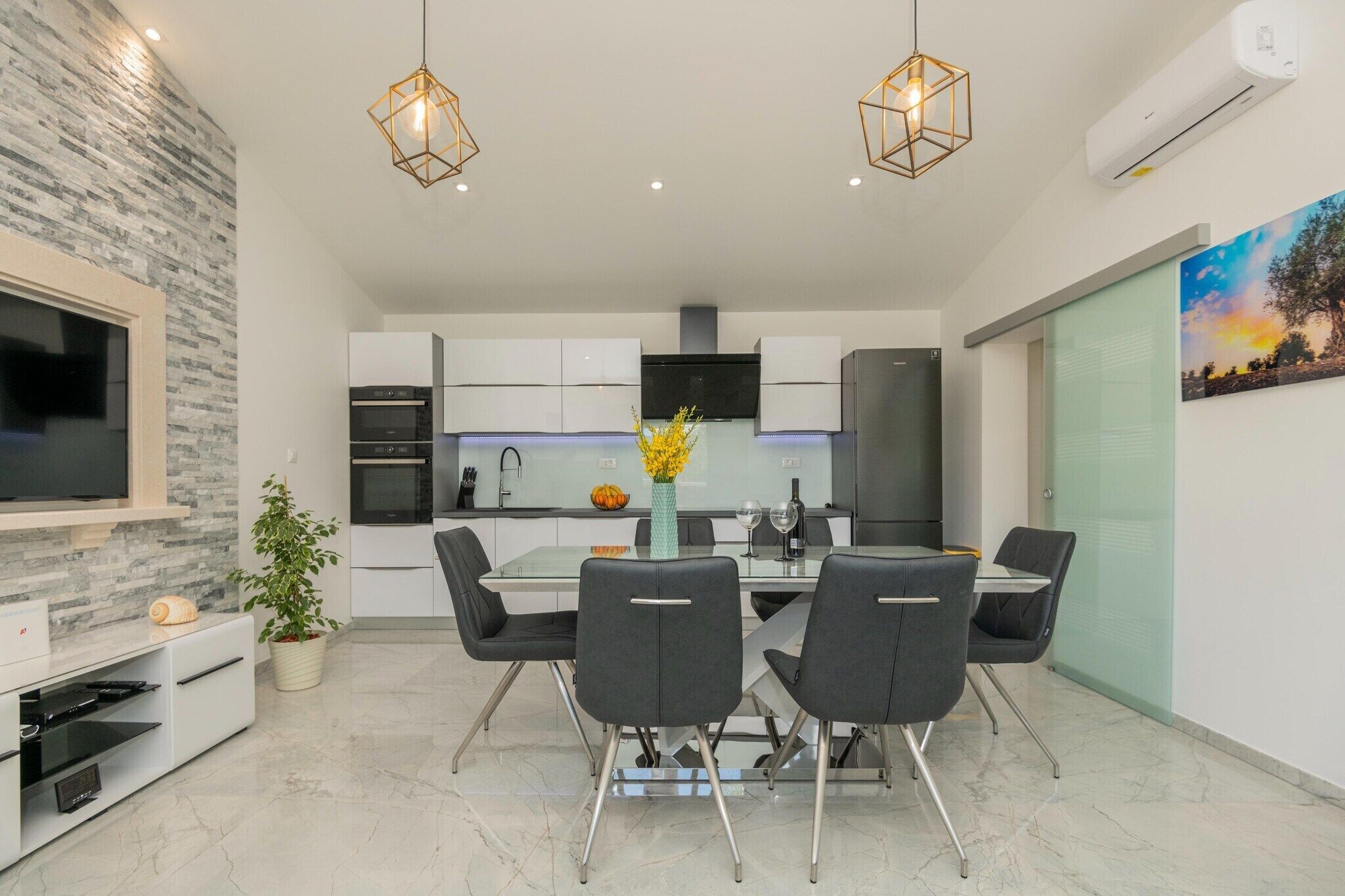 A modern kitchen with white cabinets, a central island, and a dining area with a glass table and black chairs.