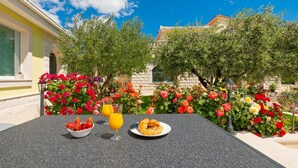 A table with a bowl of strawberries, a plate of croissants, and a glass of orange juice, set against a backdrop of colorful flowers and a clear blue sky. - Tranquil Country Villa in Naklice (županija,)