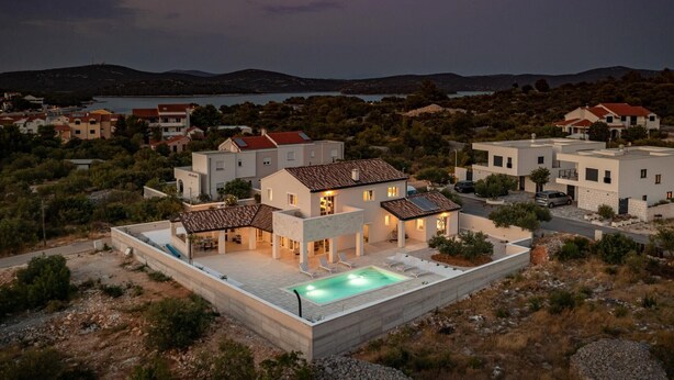 A modern villa with a swimming pool, surrounded by hills and a lake.