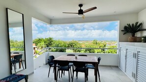 A balcony with a table and chairs, a ceiling fan, and a view of greenery and buildings. - 2 bedroom apt at blue bay resort / 5 min walk from beach / pool / private patio (Willemstad)