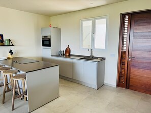 Eine moderne Küche mit einer zentralen Kochinsel, Barhocker, einem Backofen und einem Fenster über der Spüle.