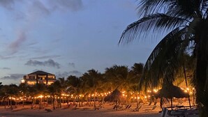 A beach with palm trees, a thatched-roof hut, and string lights. - 2 bedroom apt at blue bay resort / 5 min walk from beach / pool / private patio (Willemstad)