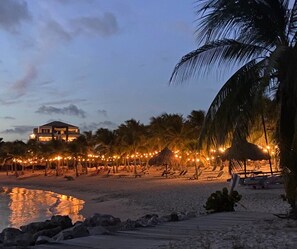 Ein Strand mit Palmen, einer strohgedeckten Hütte und Lichterketten.