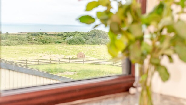 A view through a window of a rural landscape with a wooden fence, hay bales, and greenery. - 2 Bed in Stibb (oc-m30911) (Stibb)