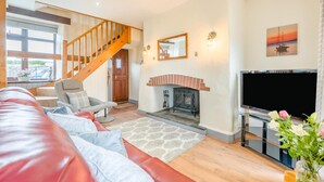 A spacious living room with a red leather sofa, a fireplace, a TV, and a staircase leading to another room. - 2 Bed in Stibb (oc-m30911) (Stibb)