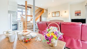 A dining area with a wooden table set for a meal, a red leather couch, and a staircase leading to another level. - 2 Bed in Stibb (oc-m30911) (Stibb)