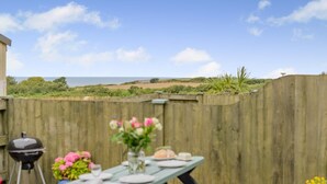 A patio with a table set for dining, a grill, and a view of the sea. - 2 Bed in Stibb (oc-m30911) (Stibb)