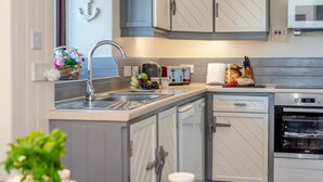 A modern kitchen with grey cabinets, a built-in dishwasher, a microwave, and a toaster. - 3 Bed in Bude (oc-d30897) (Stibb)