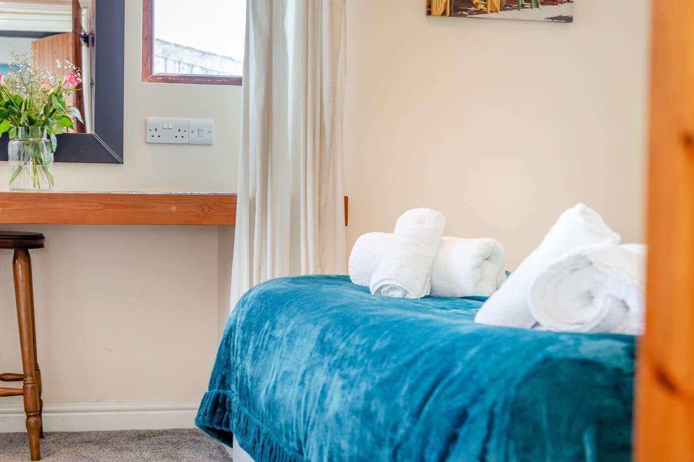 Una habitación de hotel con una cama, un escritorio de madera, un jarrón con flores y una ventana con cortinas.