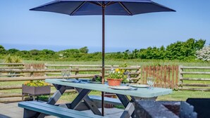 A picnic table with a blue umbrella, a potted plant, and a bottle of wine. - 3 Bed in Bude (oc-d30897) (Stibb)