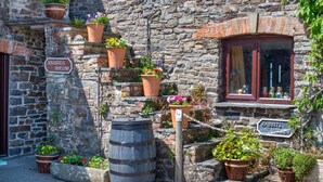 A stone building with terracotta pots on the steps, a wooden barrel, and signs indicating 'SQUIRRELS HOLLOW' and 'RABBITS WAPEN'. - 3 Bed in Stibb (oc-s30912) (Stibb)